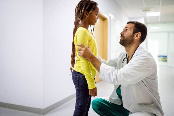 Male doctor having conversation with sad little girl at the hospital. Doctor consoling child - Valokuva, kuva