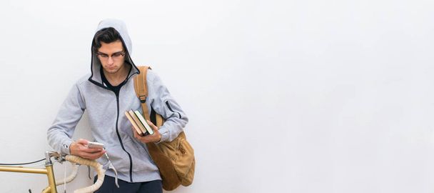 estudiante con teléfono móvil y bicicleta con libros y mochila sobre fondo blanco
 - Foto, imagen