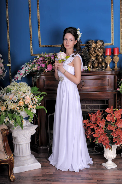 young brunette princess girl in a white elegant dress among the flowers in the room - Fotó, kép
