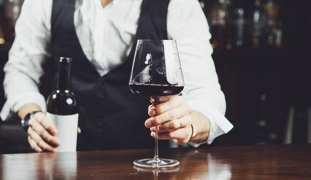 Sommelier holds out a glass of red wine at the bar, close-up. - Фото, зображення