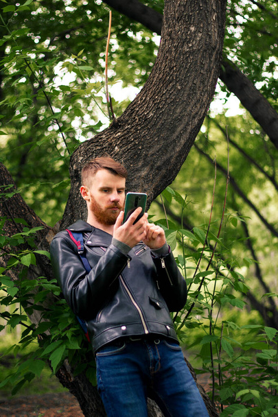 Stylish guy leafs through the news feed on the phone while standing in the middle of the forest. - Photo, image