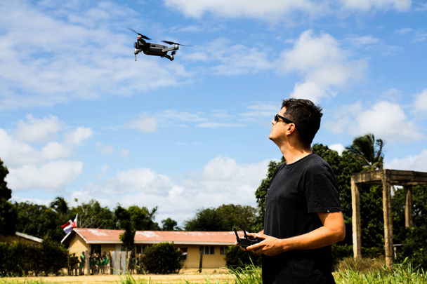 Mann fliegt eine Drohne in der Nähe einer Schule mit Kindern im Hintergrund aus dem Fokus - Foto, Bild