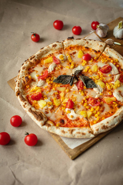 Pizza-Nahaufnahme mit Hühnchen, Tomaten, Ananas, Käse auf Kraftpapier oder Holz. Frische Pizza. - Foto, Bild