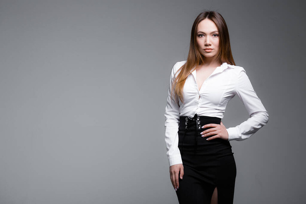 Portrait of a red-haired serious business French woman in a white shirt and black skirt on a gray background. - Fotoğraf, Görsel
