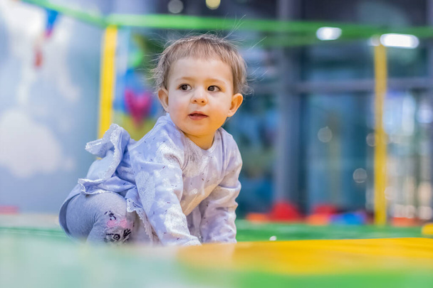 Porträt eines niedlichen Kleinkindes, das auf einem Trampolin sitzt und zur Seite schaut. Haare, die in verschiedene Richtungen herausragen, elektrisiert. Nahaufnahme, weicher Fokus, unscharfer Hintergrund - Foto, Bild