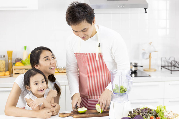 Boldog ázsiai családot a konyhában. Apa, anya és lánya készítik a salátát turmixgépben Menü ízletes smoothie és összetevők az asztalon otthon. Főzés élelmiszer, egészséges étel koncepció - Fotó, kép