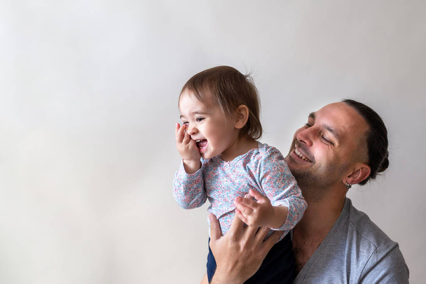 Lunghi capelli padre sorridente e tenendo la sua piccola figlia felice da vicino. Catturato su sfondo bianco studio
 - Foto, immagini