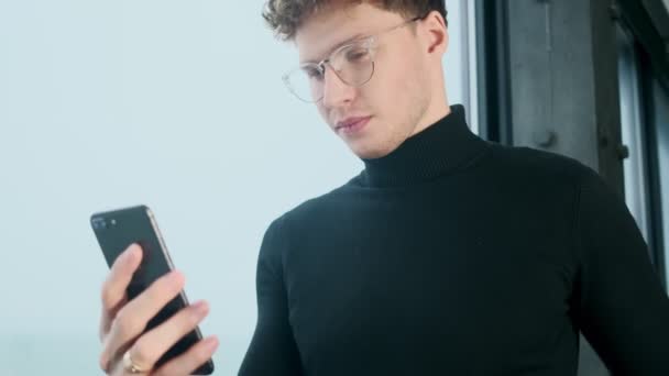 Όμορφος συγκεντρωμένος νέος επιχειρηματίας σε εσωτερικούς χώρους στο γραφείο χρησιμοποιώντας το κινητό τηλέφωνο - Πλάνα, βίντεο