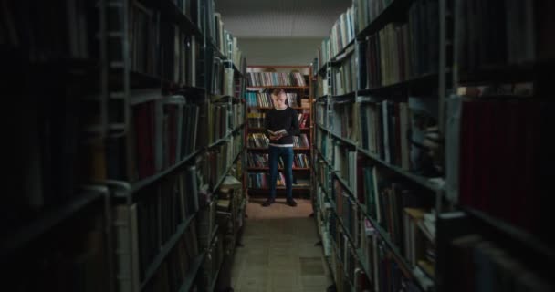 Facet stoi między półkami z książkami w świetle z okna i czyta książkę. 4k - Materiał filmowy, wideo