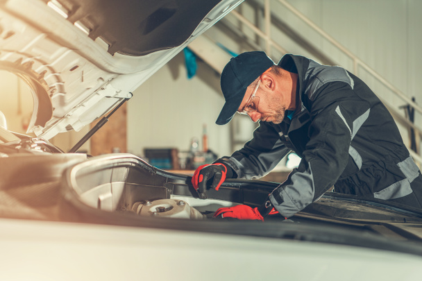 Männlicher Kfz-Techniker überprüft und fixiert Komponenten unter der Haube bei Auto Repair Workshop.  - Foto, Bild