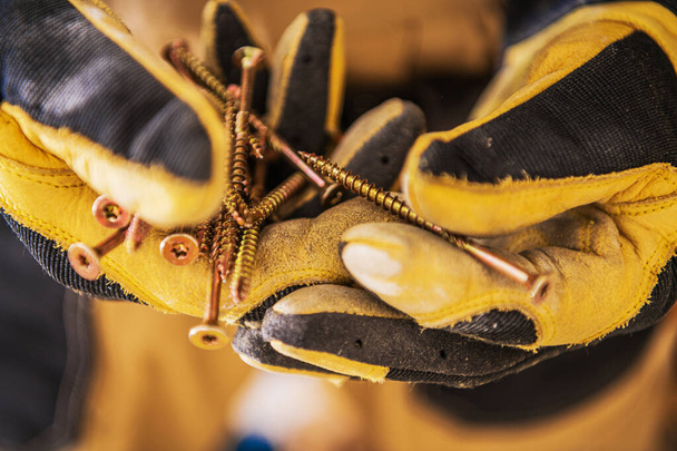 Close Up de mãos de trabalhador de construção em luvas segurando um monte de parafusos longos dourados
.  - Foto, Imagem