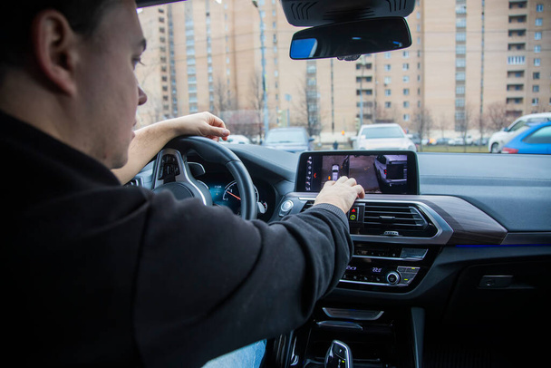 Tanımlanamayan bir adam, modern bir arabayı ekrandaki kamerayla sürüyor ve park ediyor. Modern teknolojiler, sürüş güvenliği. Yakın plan, arka plan bulanık. park desteği. - Fotoğraf, Görsel
