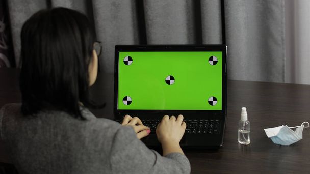 Kadın dizüstü bilgisayarda yeşil ekranlı, krom tuşlu yazılar yazıyor. Uzaklık çalışması - Fotoğraf, Görsel