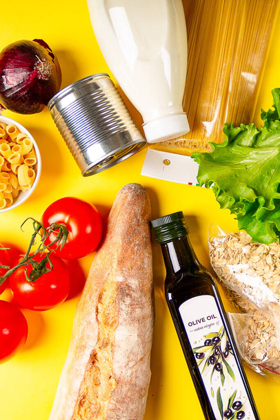 黄色の背景に様々な健康食品、トマト、パン、パスタ、オリーブオイルや野菜。食品の配送と寄付のコンセプト. - 写真・画像