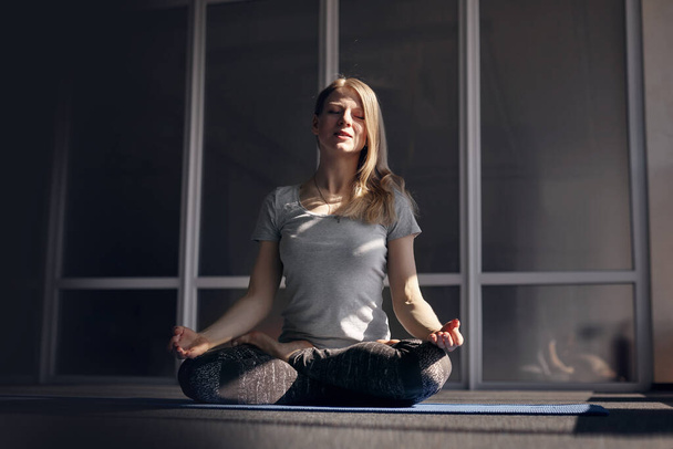 Een aantrekkelijk blond meisje in sportkleding mediteert tijdens yogales. Het concept van een gezonde levensstijl. Vooraanzicht - Foto, afbeelding