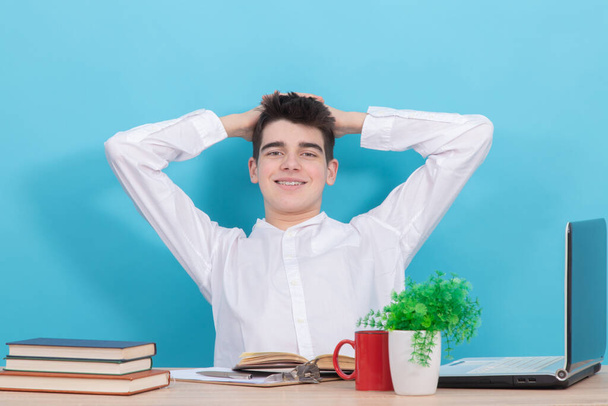 student with calm expression with hands on head sitting at desk - Photo, Image