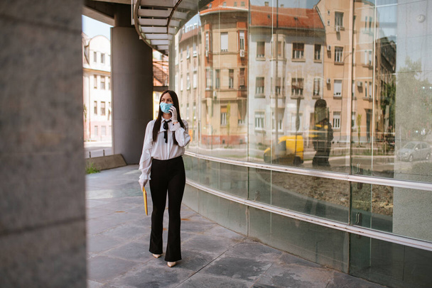 Une belle femme d'affaires caucasienne attrayante avec un masque se tient devant la société. COVID - 19 protection contre les virus
 - Photo, image