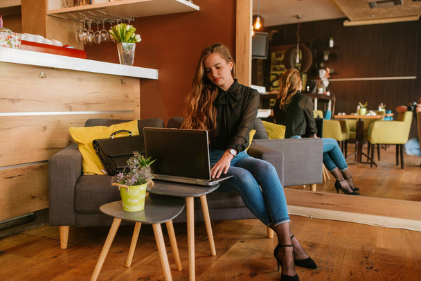 Une belle jeune femme d'affaires caucasienne est assise dans un café, buvant du café et travaillant sur un ordinateur portable. Travailler dans un café
 - Photo, image