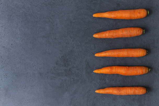 La zanahoria fresca jugosa yace en una mesa de hormigón gris. Cinco zanahorias yace en una mesa en una fila. Vista superior. Lugar vacío
. - Foto, imagen