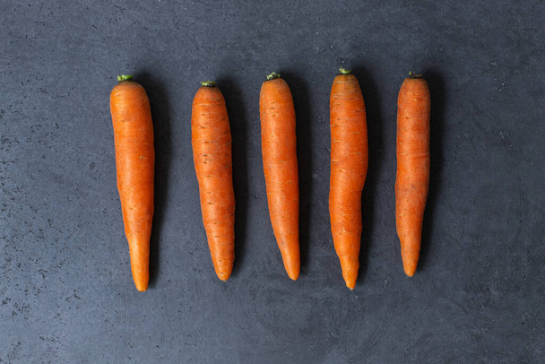 Flat lay composition with ripe fresh carrots on a gray concrete table. Fresh orange carrot. Top view. - Photo, image