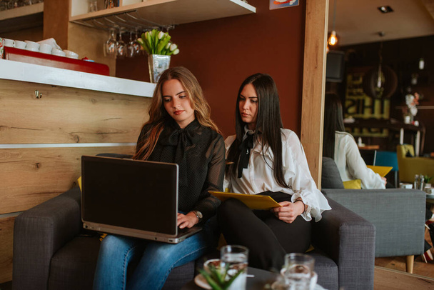 Dos hermosas mujeres de negocios están sentadas en un café, usando un teléfono y una computadora portátil. Trabajar en una cafetería
 - Foto, imagen