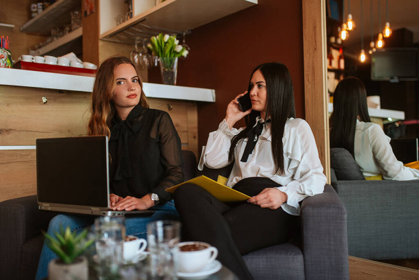 Deux belles femmes d'affaires caucasiennes sont assises dans un café, en utilisant un téléphone et un ordinateur portable. Travailler dans un café
 - Photo, image