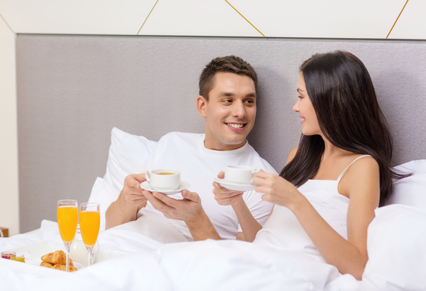 uśmiechający się para o śniadanie w łóżku w hotelu - Zdjęcie, obraz