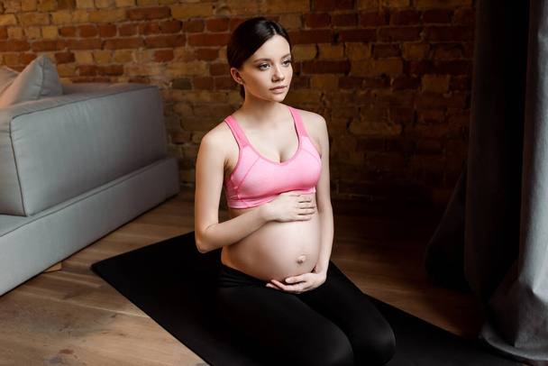 terhes nő ül fitnessz szőnyegen és megérinti has - Fotó, kép