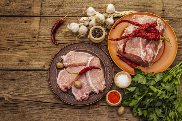 Rozmanité syrové vepřové maso. Čerstvé hřbety, koření, voňavá zelenina a petržel. Vintage dřevěné desky stůl, pohled shora - Fotografie, Obrázek