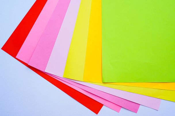 Vellen felgekleurd kantoorpapier worden van bovenaf op een witte achtergrond gefotografeerd. Rood, roze, paars, geel, oranje, groen - Foto, afbeelding