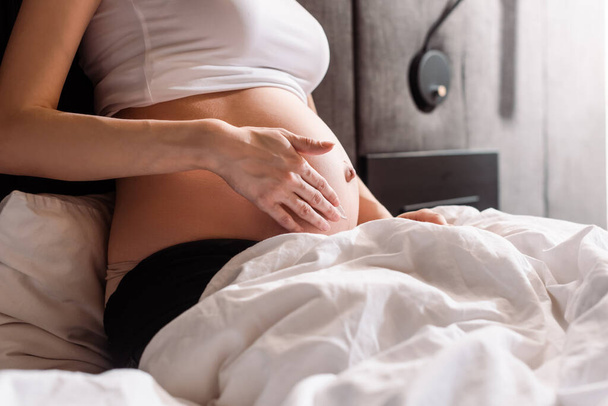 cropped view of pregnant woman touching belly with gel in bedroom  - Foto, afbeelding