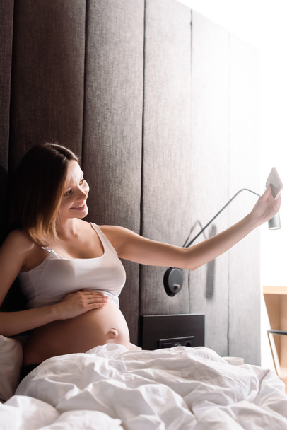 весела вагітна жінка приймає селфі в спальні
  - Фото, зображення