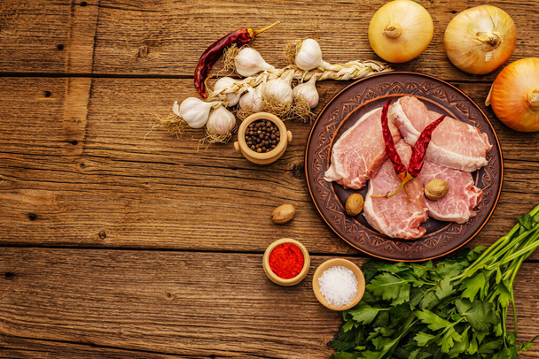 Carne de cerdo cruda. Lomo fresco, especias, verduras aromáticas y perejil. Mesa de madera vintage, vista superior
 - Foto, Imagen