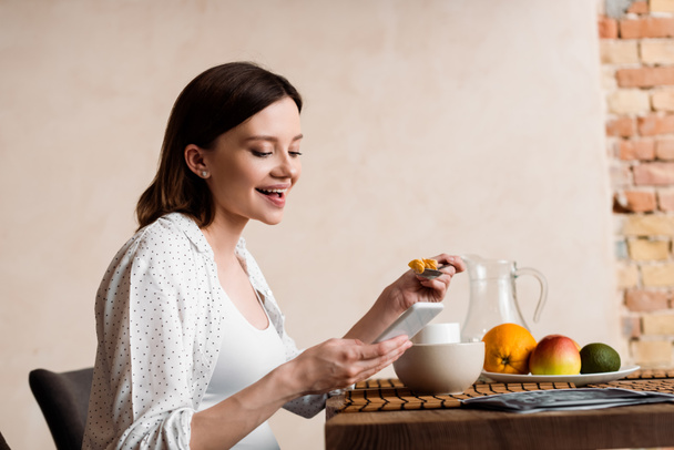 happy and pregnant woman using smartphone near tasty breakfast  - Photo, Image
