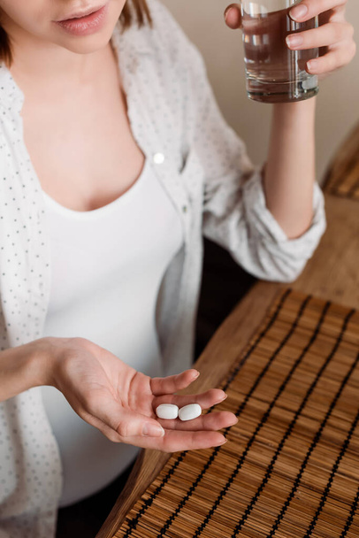 bijgesneden weergave van zwangere vrouw met vitaminen pillen en glas water  - Foto, afbeelding