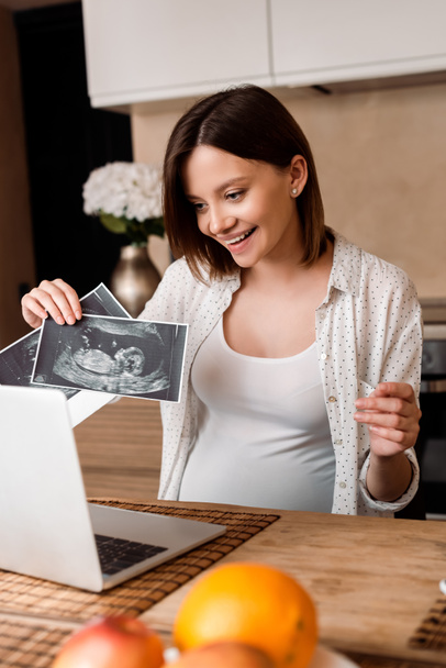 selective focus of happy pregnant woman showing ultrasound photos while having video call  - Foto, Imagem