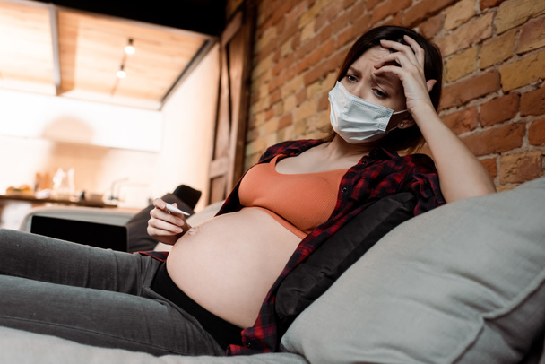 sick and pregnant woman in medical mask holding digital thermometer  - Photo, Image