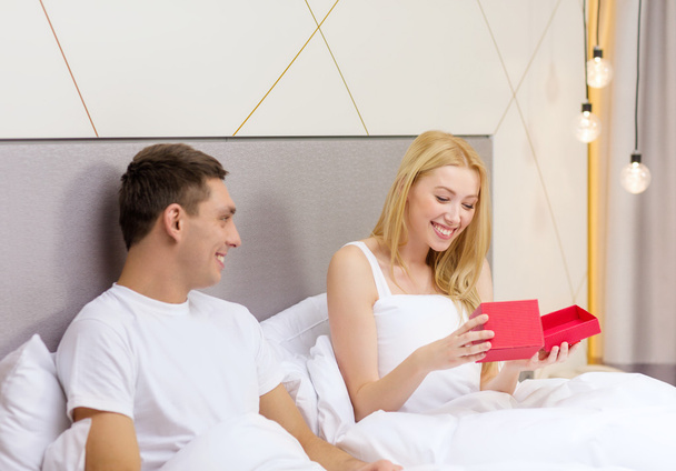 Smiling couple in bed with red gift box - Zdjęcie, obraz