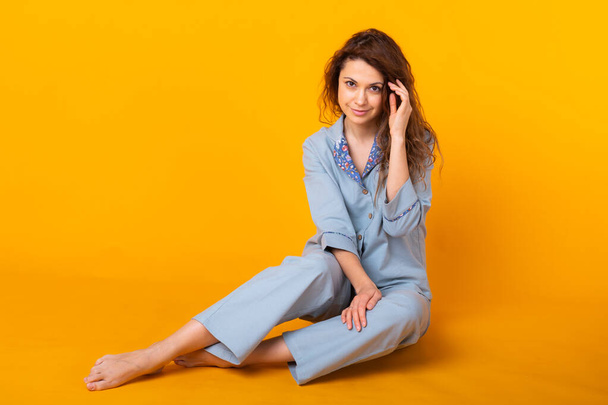 Sluit een jonge vrouw in blauwe huiskleding. Geïsoleerd op gele achtergrond. Pajama-concept. - Foto, afbeelding