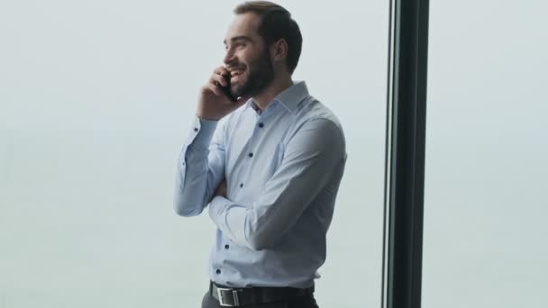 Handsome cheerful pleased young business man indoors in office talking by mobile phone - Video, Çekim