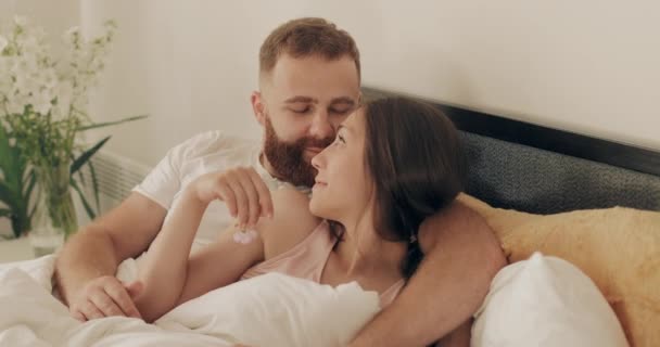 Romantic couple cuddling and smiling while lying on bed early morning. Man and woman in love having good time together embracing and looking in eyes. Concept of happy relationship. - Metraje, vídeo