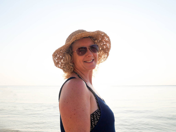 Portrét staré ženy v klobouku a slunečních brýlích na pobřeží za slunečního světla - Fotografie, Obrázek