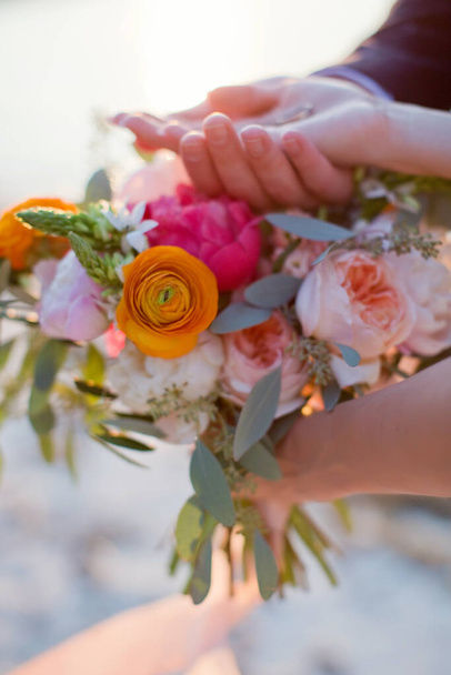 Wedding rings in the couple hands. Hands with rings and wedding colorful bouquet - Foto, Imagen