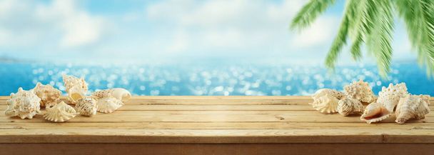 Summer background with wooden table, seashells nad palm tree over sea beach bokeh - Фото, изображение