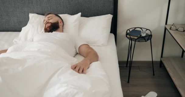 Shocked young good looking man oversleep and getting up very fast while lying in bed . Handsome bearded guy waking up and screaming while realising oversleep work in morning. - Felvétel, videó