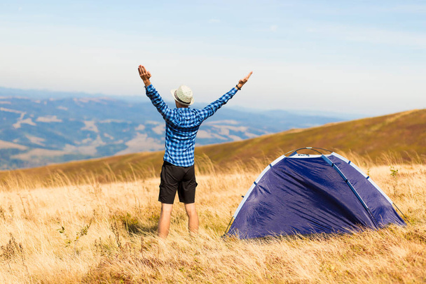 Back view of happy traveler man on top of mountain raised hands enjoying freedom and view near tent camping outdoor. Travel adventure lifestyle success concept, hiking active vacations - Zdjęcie, obraz