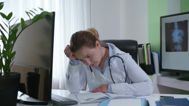 medico donna stanca tiene la testa in mano, si sente male a causa di malattia o stanchezza, lavora al computer e guarda il monitor mentre seduto in sala medica
 - Filmati, video