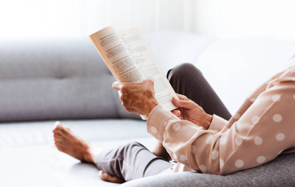 Middle-aged brunette woman on the gray sofa reading book, soft focus, stay at home concept, cozy background - Foto, immagini