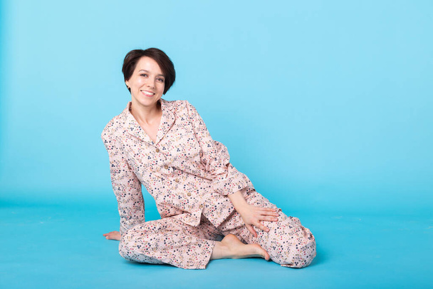 Rapariga sorridente em pijama casa desgaste posando enquanto descansa em casa isolado no fundo azul estúdio retrato. Relaxe conceito de estilo de vida de bom humor
. - Foto, Imagem