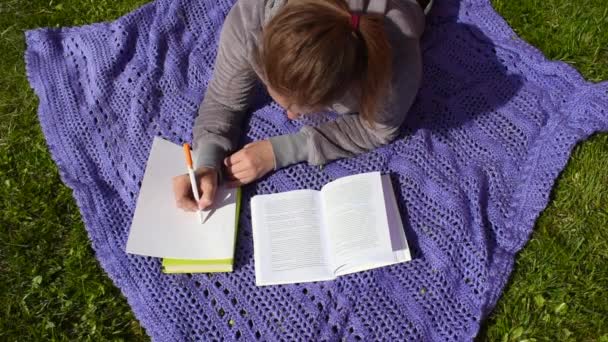 Girl on a blanket in the garden studying the lessons. Distance learning outdoor - Footage, Video